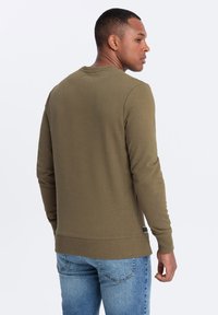 Felpa a maniche lunghe verde oliva, in misto cotone, collo a giro, polsini e orlo a coste, texture liscia, presenta un'etichetta con logo sul lato.