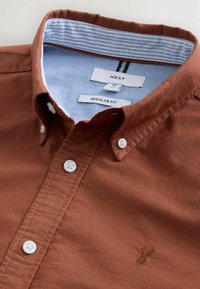Camicia marrone a maniche lunghe, dalla vestibilità regolare, con bottoni bianchi, un colletto foderato a strisce blu e un piccolo logo ricamato sul petto.