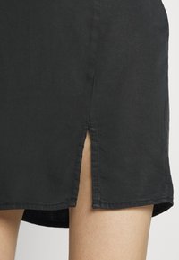 Saia preta com abertura lateral, feita de tecido leve. A bainha é costurada de forma neat, com uma textura suave e um corte reto.