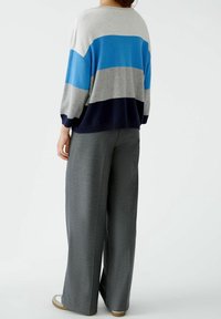 Sweter w paski wykonany z dzianiny w kolorach szarym, jasnoniebieskim i granatowym, zestawiony z szerokimi szarymi spodniami i beżowymi butami.