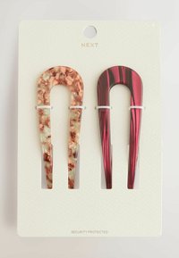 Deux barrettes sur une carte : l'une en plastique marbré marron et vert, l'autre en rouge brillant avec des rayures noires. Chacune présente un design en forme de U.