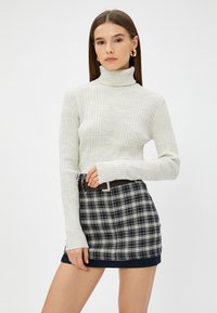 Crème ribbeltrui met col en lange mouwen, gecombineerd met een marineblauw en wit geruit mini-jurk met een zwarte riem tailleband.