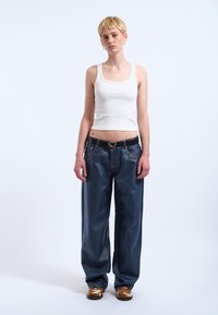 Vit ribbad linne, oversized mörkblå denimbyxor, svart bälte med hjärtformat spänne, och mönstrade bruna skor.
