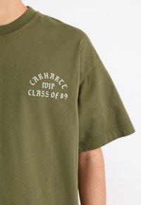 Camiseta de algodón de manga corta en verde oliva con texto blanco: "Carhartt WIP Clase del 89" en un diseño curvado en el pecho.