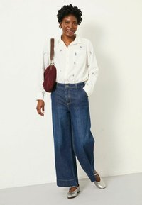 White button-up shirt with small embroidered anchor patterns, paired with wide-leg blue denim pants and metallic silver flat shoes.