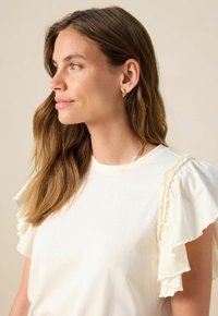 Helles cremfarbiges T-Shirt mit Rüschen, geschichteten Ärmeln und rundem Halsausschnitt. Sanfte Textur mit dezentem Fall, ohne sichtbare Muster oder Akzente.