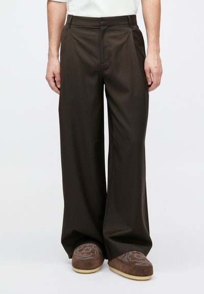 Pruunid laia säärega püksid, millel on sile tekstuur, keskmise kõrgusega vöökoht ja sirge lõige. Sobitatud tumepruunide tikanditega sussidega.