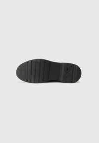 Black rubber shoe sole with textured surface, featuring horizontal grooves for grip and a stamped logo, rounded toe shape.