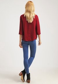 Maglietta borgogna a tre quarti con una vestibilità ampia, abbinata a jeans skinny blu e stivaletti neri con tacco largo.