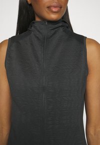 Chaleco sin mangas negro con patrón texturizado, cuello alto y cremallera frontal. Tejido suave con acentos en los hombros en contraste.