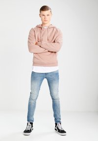 Lys rosa hettegenser med snor, lagd over en hvit skjorte. Brukt med slitte lyseblå jeans og svarte høye sneakers.