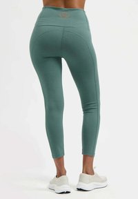 Hoch taillierte Leggings aus weichem, tealfarbenem Stoff mit schlankem Schnitt. Verfügen über ein dezentes Lotus-Logo auf der Rückseite und eine glatte, dehnbare Textur.