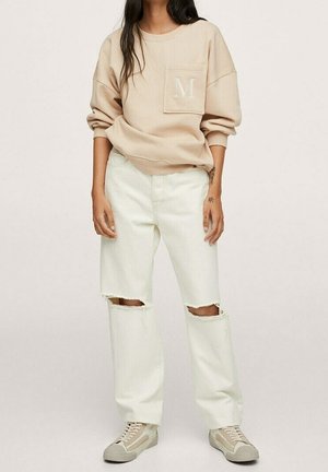 Felpa color beige chiaro con tasca frontale e ricamo "M." Abbinata a jeans strappati color bianco sporco e sneakers beige. Stile piatto e casual.