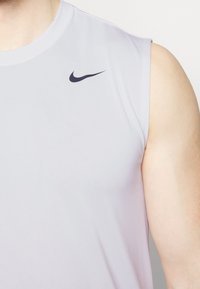 Light gray sleeveless athletic top, made of smooth fabric. Features a small black Nike logo on the left shoulder.