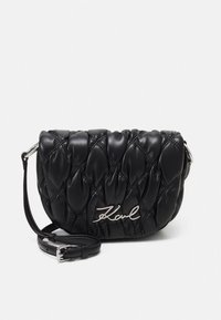 Crna torba preko ramena od prošivene kože s srebrnim potpisnim logotipom, podesivim remenom i jastučićastom teksturom. Kompaktan dizajn za nošenje najosnovnijih stvari.