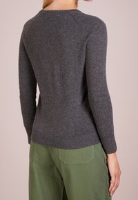 Grå stickad tröja med rund halsringning och långa, figurnära ärmar. Den har en ribbad fåll och raglanärmar, i kombination med gröna byxor.