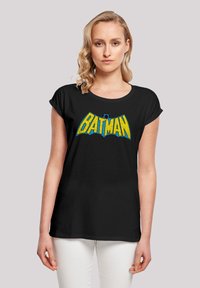 Must mustvalge T-särk, millel on suur kollane ja sinine "BATMAN" logo rinnal, lühikesed volditud varrukad ja lahtine lõige.