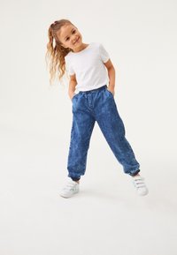 Tummansiniset denim-jogger-housut, joissa on joustava vyötärö ja hihansuukkeet, yhdistettynä yksinkertaiseen valkoiseen lyhythihaiseen t-paitaan ja valkoisiin lenkkareihin.