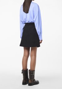 Vaaleansininen pitkähihaisen paidan, mustan A-linjaisen hameen ja ruskea nilkkurit, joissa on soljet ja tekstuuri. Takaviisto.