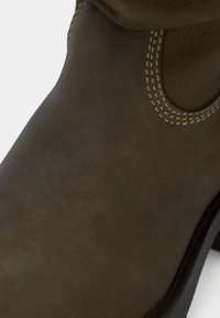 Bottine en cuir marron avec une texture lisse, présentant des coutures contrastées et un design à bout rond. La tige comprend un détail en forme de découpe circulaire.