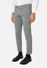 Chinos in cotone grigio con vestibilità slim, caratterizzati da una chiusura con un solo bottone e tasche, abbinati a mocassini neri e calzini scuri.