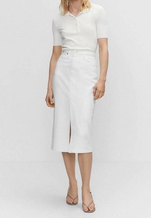 Vrouw draagt een wit polo-shirt met korte mouwen, ingestopt in een witte midi-rok met hoge taille en een voorsplit, gecombineerd met grijze open-toe sandalen met hak.