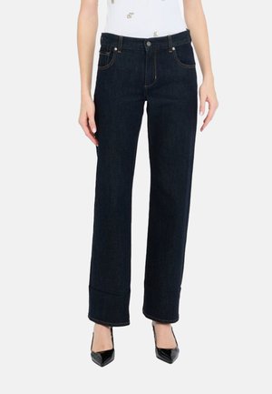 Jeans in denim scuro con un design a gamba dritta, caratterizzati da cuciture dorate, passanti per cintura e tasche frontali. Indossati con tacchi neri a punta.