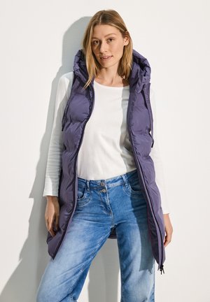 Purple padded vest with a hood, featuring a front zip, side pockets, and a long design. Underneath is a white long-sleeve shirt and blue jeans.