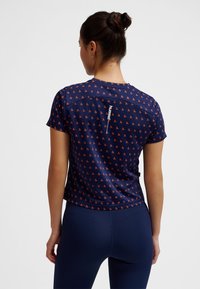 Marinblå sporttröja med mönster i små orange detaljer, korta ärmar och en synlig logotyp på baksidan, tillverkad i lätt tyg.