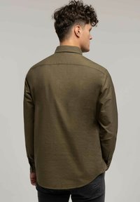 Oliwkowa koszula z długim rękawem, z kołnierzem zapinanym na guziki i prostym dołem. Posiada mankiety z guzikami oraz miękką, teksturowaną tkaninę.