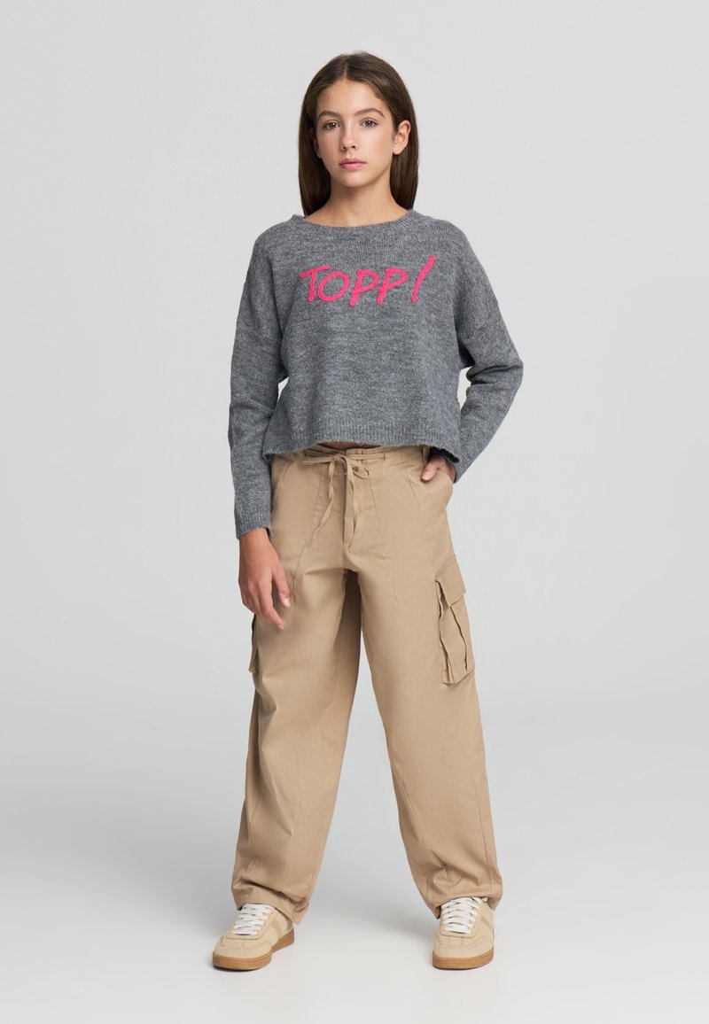 Maglione corto grigio con ricamo rosa "TOPP!", abbinato a pantaloni cargo beige larghi con tasche laterali e vita con coulisse.