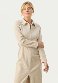 Rochie din bumbac bej cu guler, mâneci lungi, închidere cu fermoar frontal și fanta pe lateral, având o textură ribonată și o croială ajustată.