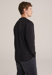 Juoda ilgomis rankovėmis medvilninė palaidinė su tiesiu kirpimu ir apvalia iškirpte, derinama su tamsiais džinsais. Paprastas ir minimalistinis dizainas.