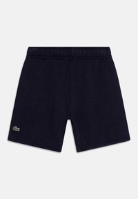 Short bleu marine à taille élastique avec petit logo crocodile vert sur la jambe gauche, fond de surface plate.