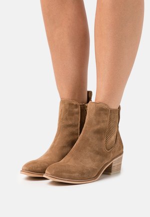 Bottines en suède marron avec un bout arrondi, des perforations sur les côtés, une fermeture éclair et un talon empilé.