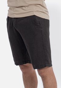 Czarne lniane szorty o luźnym kroju, z bocznymi kieszeniami i dołem, który kończy się tuż powyżej kolan. Miękka faktura z minimalnymi zagnieceniami.