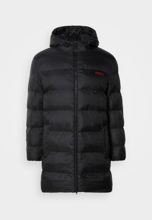 Must mustraamjak, millel on kapuuts, ees on lukuga ja horisontaalselt quiltitud disain. Punane brändi logo on nähtav vasakul rinnal.