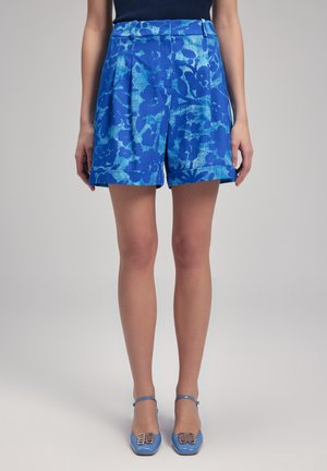 Blauwe shorts met bloemenprint en plooien, gemaakt van lichtgewicht stof. Heeft omgeslagen zomen en zijzakken. Gecombineerd met blauwe hakken.