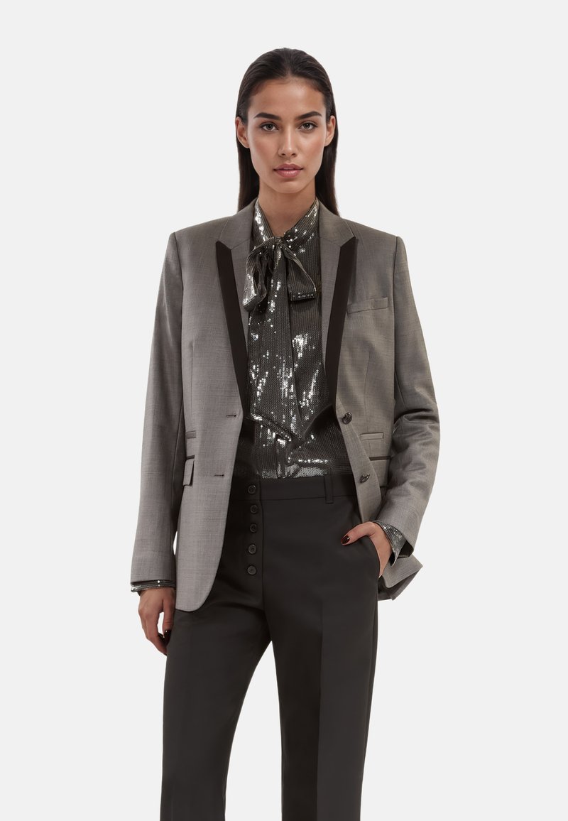 Strukturierter grauer Blazer mit schwarzen Revers, kombiniert mit einer glänzenden, paillettenbesetzten schwarzen Bluse und maßgeschneiderten schwarzen Hosen mit Knopfdetails.