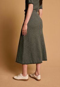 Robe midi tricotée verte avec des manches courtes et un ourlet évasé, assortie à des baskets blanches. Le tissu a une finition texturée.