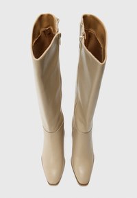 Beige Leder kniehohe Stiefel mit glatter Textur, spitzem Schuhkopf und zwei Reißverschlüssen an der äußeren Welle. Flacher Absatz für Stabilität.