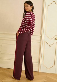 Bordové široké kalhoty s červenými bočními pruhy v kombinaci s topem v burgundské a bílé pruhy. Měkká tkanina s volným střihem a elastickým pasem.