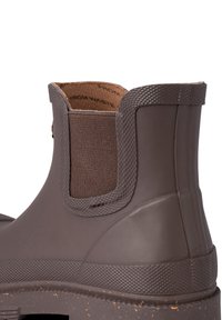 Bottine en caoutchouc marron avec des panneaux latéraux élastiques, semelle texturée et finition lisse. Elle possède une doublure intérieure rugueuse et une forme arrondie.