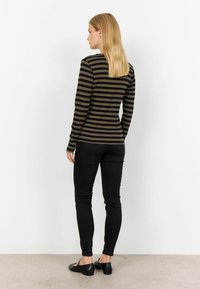Langsleeve gestreepte top in olijfgroen en zwart, gecombineerd met zwarte skinny jeans en platte zwarte schoenen. Glad materiaal met een aansluitende pasvorm.