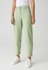 Pantalons en coton vert clair avec une coupe décontractée, dotés de grandes poches avant et de revers roulés, associés à des baskets blanches.