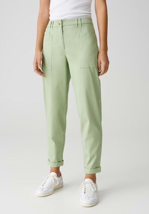 Pantaloni in cotone verde chiaro con una vestibilità rilassata, caratterizzati da ampie tasche frontali e orli arrotolati, abbinati a sneakers bianche.
