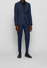 Námořnický modrý kostým s kostkovaným vzorem vyrobený z látky s hladkou texturou, vypasovaná silueta, zapínání na jeden knoflík, doplněný o elegantní černé boty.