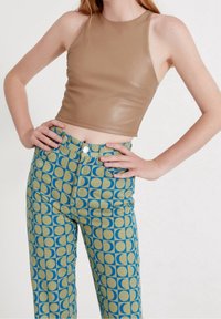 Top court sans manches marron en tissu lisse, associé à un pantalon taille haute avec un motif circulaire bleu et vert.