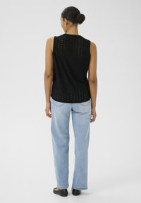Top sans manches noir avec un design à œillet et un col rond, associé à un jean droit bleu clair et des chaussures plates noires.