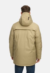 Beige boblejakke med hette, med en baklodddesign og sidelommer, laget av et glatt, vanntett materiale.